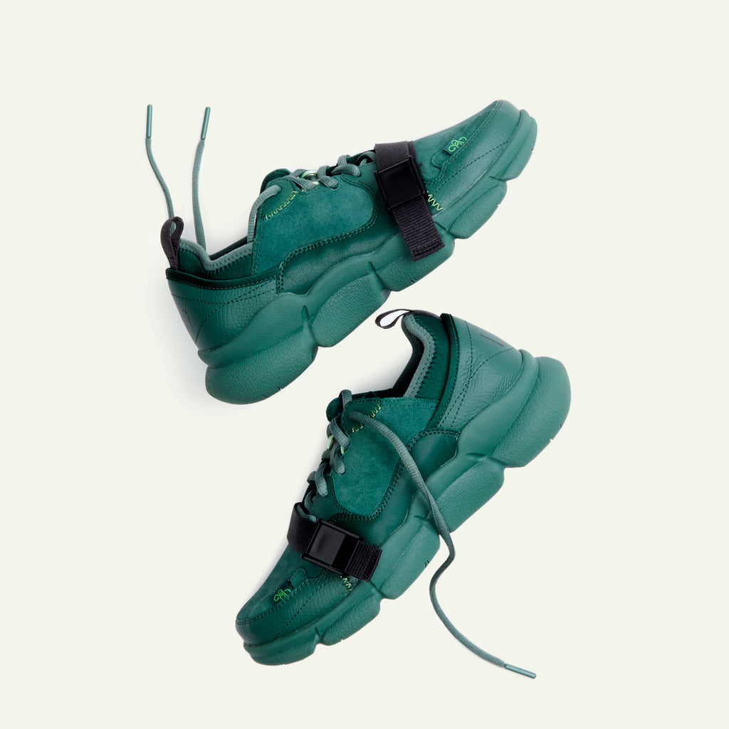 A pair of Caudal Lure sneakers in the color Concrete Jungle Green. The sole uses a Vibram tooling called Plump in the Pantone color Duck Green. The upper materials are made up of various shades of green in the materials suede, pebbled leather and neoprene. The Lilith NYC wordmark logo is printed at the back of the sneaker.